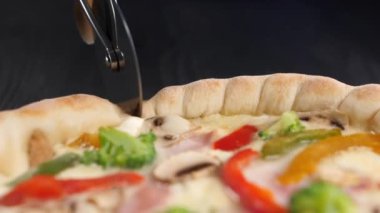 Yuvarlak pizza bıçağı taze bir pizzanın yüzeyinde yuvarlanır ve keser. Tekerlek vitrininde kırmızı biber, brokoli, peynir, jambon. Kapat..