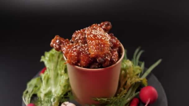 黑色背景 香喷喷的鸡翅倒入酱汁中 用纸桶将芝麻籽和蔬菜一起撒在石盘上 — 图库视频影像