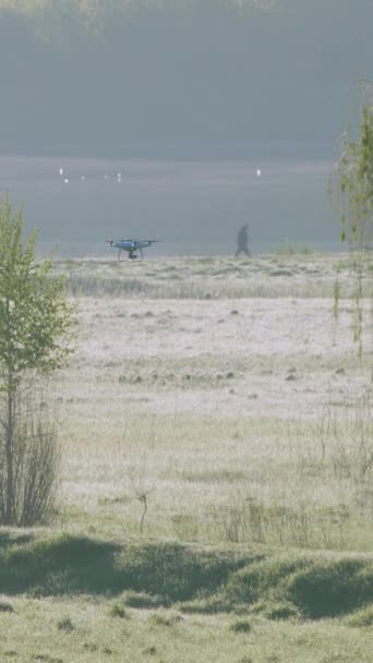 垂直录像 一只白色的四足动物在夏天的风景中飞翔 清晨的露珠和大雾笼罩在河边 一个人沿着河岸散步 无人机跟着那个人 — 图库视频影像