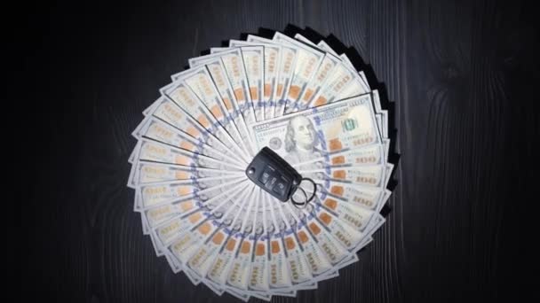 100美元的钞票折叠成圆形 在一张黑色桌子的木制表面上旋转 在钱的中间是一把汽车钥匙 汽车贸易概念 — 图库视频影像