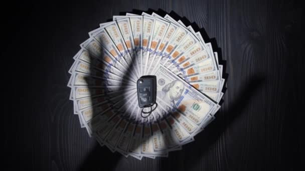 一百美元的钞票堆在一张木制桌子表面上 呈圆形 在钱的中间是汽车上的一个关键的雾气 手的影子试图拿走所有的现金和钥匙 — 图库视频影像