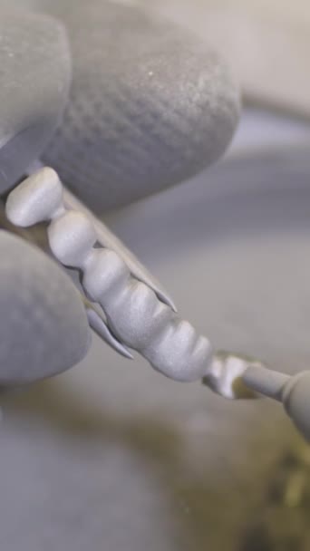 垂直录像 牙科技师在牙科实验室用喷砂器抛光人造陶瓷牙 专业人员手拿着假牙 戴着手套 用沙子擦拭 — 图库视频影像