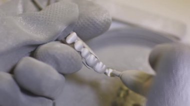 Diş laboratuarında kum blaster kullanarak yapay seramik dişleri parlatma diş teknisyeni. Profesyonel elinde sahte dişler tutarak ve kum blaster ile parlatma sırasında eldiven giyiyor.
