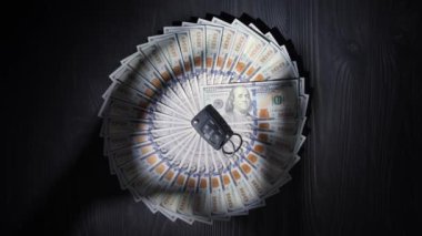 100 dolarlık banknotlar ahşap bir masa yüzeyinde daire şeklinde uzanır. Paranın ortasında, arabadan alınmış bir anahtarlık var. Ellerin gölgeleri tüm parayı ve anahtarı almaya çalışır..