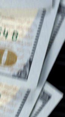 Dikey video. Yüzlerce dolarlık banknotların aşağıya doğru hareket etmesi makroda siyah bir arka planda, ekranda 100 numara var. Paranın ön sağ tarafı. Yatırım konsepti, zenginlik.