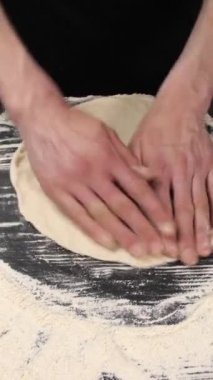 Dikey video. Restoranda İtalyan pizzası pişirmek. Ellerinle çiğ pizza hamuru uzatıyorsun. Profesyonel bir aşçı elleriyle İtalyan pizza hamurunu gerer ve büker..