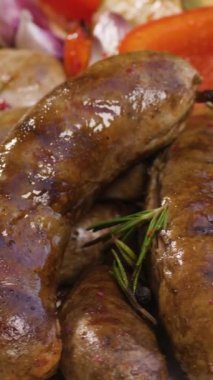 Dikey video. Fırında kabak, domates, sarımsak, paprika ile ızgara sosis yemeye hazır. Pita ekmeğinin üzerinde duran tabakta sosisten sebzeye kadar yiyecekler çeşitlidir..