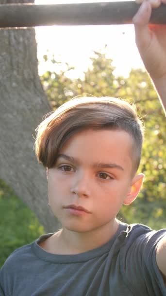 バーティカルビデオ 10代の少年は スイングスティックの端に保持し 意図的にカメラに向かいます 夜の太陽の後ろに 幼少期からの記憶の概念 — ストック動画
