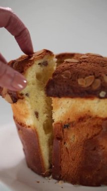 Dikey video. Bir kadın eli, paskalya pastasından bir parça alır ve hamurun kalitesini göstermek için bir tabağa koyar. Kuru üzümlü ve şekerli meyveli hamuru kapat..