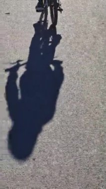 Dikey çekim. Gri asfaltta bisiklet süren ve pedal çeviren bir çocuğun gölgesi var. Mutlu çocukluk ve nostalji kavramı.