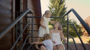 Genç bir anne, ahşap bir evin girişindeki demir bir balkonda otururken kızlarıyla konuşur. Günlük hayatta çocukluk ve annelik..