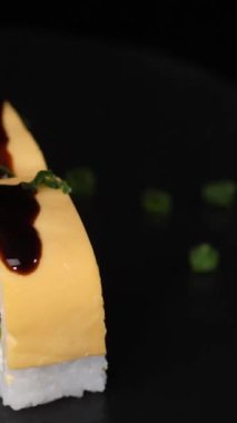 Dikey video. Somon, peynir, salatalık ve marullu taze suşi ruloları. Çanak taştan bir tahtada döndürülmüş ve üzerine siyah bir zemin serpiştirilmiş soğan serpiştirilmiş..