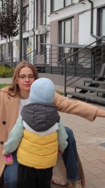 Dikey video. Krem rengi ceket giymiş genç bir anne, ona sarılarak koşan oğluyla tanışır. Şefkatli annelik ve çocuklar ailelerini severler..