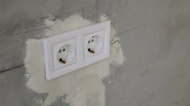 Plastik çerçevenin içindeki iki beyaz elektrik prizi gri alçılı beton bir duvara monte edilmiş. Bir odada yenileme işi kavramı.