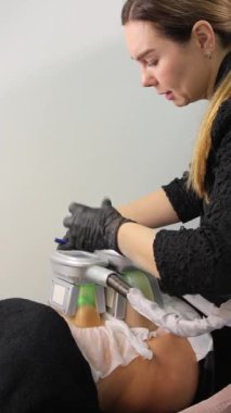 Dikey video. Kriyolipoliz uygulaması, kriyoterapi, iki tabakla hastaların karnı üzerinde işlem yapan güzellik uzmanı bir zayıflatma cihazı..