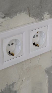 Dikey video. Plastik çerçevenin içindeki iki beyaz elektrik prizi gri alçılı beton bir duvara monte edilmiş. Bir odada yenileme işi kavramı.