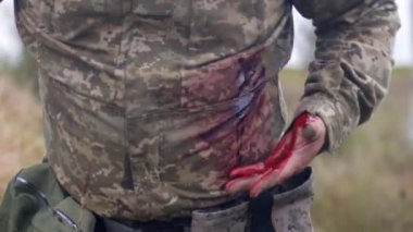 Topallayan ve sol elini kurşun yarasından akan kanın olduğu yerde tutan bir askerin yakınına. Ukraynalı bir adamın kamuflaj üniforması..