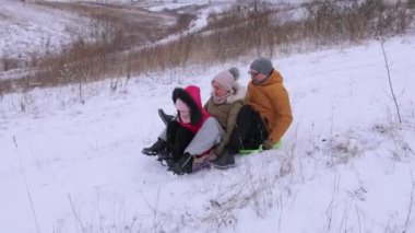 Bir ailenin plastik kızaktan aşağı inerken eğlendiği bir kar kaydırağı. Anne, kız ve baba oturur ve daha hızlı gitmek için kendilerini zorlarlar. Doğal tepelerde kış oyunları..