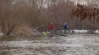 İki adam çıplak ağaçlarla çevrili sessiz bir nehirde kürek çekiyorlar. Bazı dallarda karla birlikte, sonbaharın sonlarındaki soğuk hava çok açık. Aktif spor eğlencesi.