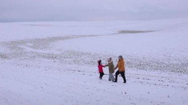 Üç kişilik bir aile, beyaz tarlalar ve bulutlu bir gökyüzü ile çevrili engin karlı bir arazide birlikte yürür. Kırmızılı çocuk yol gösteriyor, rahat bir sahne yaratıyor..