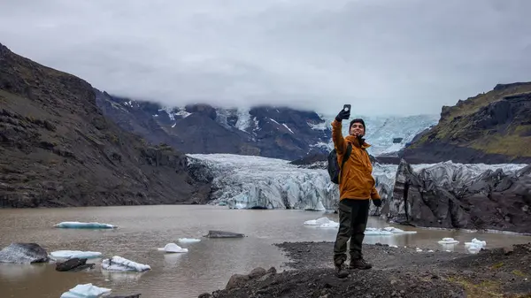İzlanda 'da arka planda bir buzulla fotoğraf çeken bir adamın fotoğrafı.