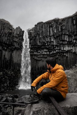 Genç Latin adam kayalıklarda oturmuş şelaleye bakıyor.