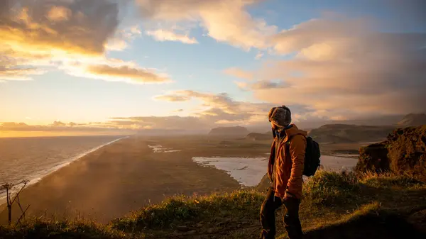 İzlanda 'daki bir dağın tepesinde gün batımında denize bakan Latin bir adam.