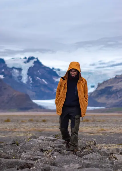 Dağlarda sarı ceketli, arka planda buzdağı olan genç bir latin.