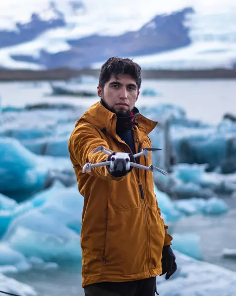 İzlanda 'da arka planda bir buzulla kameraya insansız hava aracı tutan bir adamın resmi.