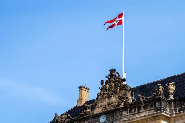 Arka planda mavi gökyüzü olan bir binanın tepesinde Danimarka bayrağı