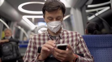 Maskeli adam Münih 'te metroya biniyor ve akıllı telefonuyla internette sörf yapıyor. Hijyen, sağlık ve enfeksiyon konsepti. Yolcu metroda seyahat ederken Coronavirus haberlerini aramak için telefonu kullanıyor. 