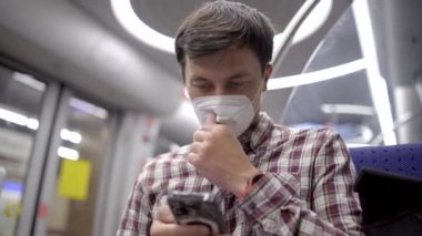 Adam akıllı telefon kullanıyor ve toplu taşıma için işe giderken maske takıyor. Yeni normal. Maskeli yolcu metroyla seyahat ediyor ve Münih 'te akıllı telefonuyla internette sörf yapıyor. 5G İnternet. 