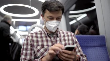 Münih metrosundaki maskeli yolcu akıllı telefonunda 5G internet kullanıyor. Almanya 'da metroda seyahat ederken cep telefonunu kullanan maskeli bir adam. Covid 'e karşı maske. Hijyen, Sağlık ve Enfeksiyon. 