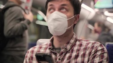 Adam akıllı telefon kullanıyor ve toplu taşıma için işe giderken maske takıyor. Yeni normal. Maskeli yolcu metroyla seyahat ediyor ve Münih 'te akıllı telefonuyla internette sörf yapıyor. 5G İnternet. 