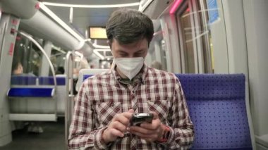 Münih metrosundaki maskeli yolcu akıllı telefonunda 5G internet kullanıyor. Almanya 'da metroda seyahat ederken cep telefonunu kullanan maskeli bir adam. Covid 'e karşı maske. Hijyen, Sağlık ve Enfeksiyon. 