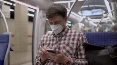 Münih metrosundaki maskeli yolcu akıllı telefonunda 5G internet kullanıyor. Almanya 'da metroda seyahat ederken cep telefonunu kullanan maskeli bir adam. Covid 'e karşı maske. Hijyen, Sağlık ve Enfeksiyon. 