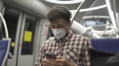 Maskeli adam Münih 'te metroya biniyor ve akıllı telefonuyla internette sörf yapıyor. Hijyen, sağlık ve enfeksiyon konsepti. Yolcu metroda seyahat ederken Coronavirus haberlerini aramak için telefonu kullanıyor. 