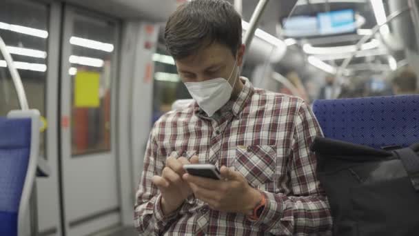 マスクマンはミュンヘンの地下鉄に乗り スマートフォンでインターネットをサーフィンします 感染の概念 乗客は地下鉄で旅行中にコロナウイルスニュースを検索するために電話を使用します — ストック動画