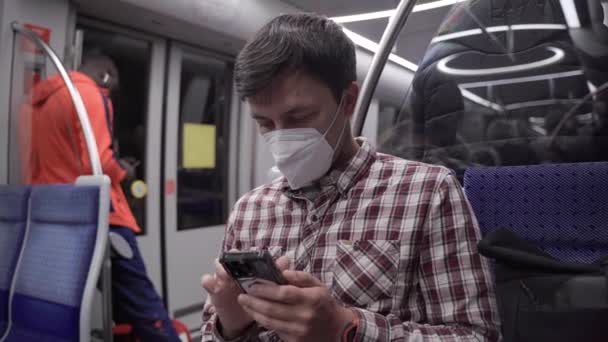 マスクマンはミュンヘンの地下鉄に乗り スマートフォンでインターネットをサーフィンします 感染の概念 乗客は地下鉄で旅行中にコロナウイルスニュースを検索するために電話を使用します — ストック動画