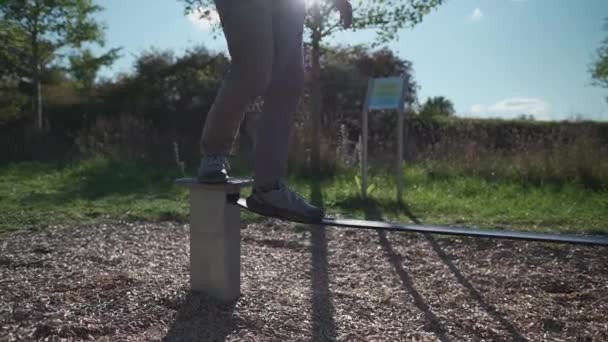靴の初心者の男性は ドイツの公園でゴム製のスラックラインの上を歩くとバランスを保つことを学びます ミュンヘンのシティジムで男は伸張ロープでバランスをとる スラッキンリン スラックライン バンド ゴムロープのバランス — ストック動画