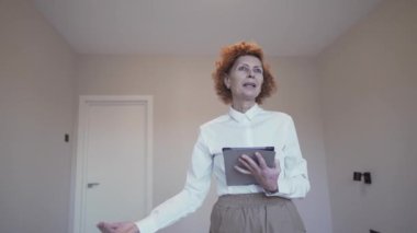 Emlakçı Showround. Kadın emlak komisyoncusu kameraya bakar ve müşteriye boş bir dairede tavsiye verir. Emlakçı daire satıyor. Satılık ve kiralık gayrimenkul teması. Daire satılıyor. 