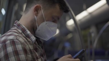 Almanya 'da koronovirüs salgını sırasında toplu taşıma ile seyahat etmek. Maskeli adam metroya biner ve akıllı telefondan internette sörf yapar. Münih Metropolitan Demiryolu. Kapalı. Burun ve ağzı kapatma kuralları