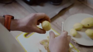 Evcil mutfakta patates soyan beyaz bir erkek. Patates temizleme. Pişirilmiş çaydanlık. Yemek hazırlama konsepti. Elinde bıçak ve patatesi tutan tanınmayan biri..