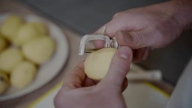 Eller, evde bir adam patatesleri bıçakla soyar. Yemek yapmak, sağlıklı yemek yemek. Sebze temizleme işlemi. Sağlıklı yemek. Taze sarı patates mutfak soyacağı soyuluyor. Yemek hazırlama..