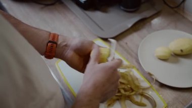Evcil mutfakta patates soyan beyaz bir erkek. Patates temizleme. Pişirilmiş çaydanlık. Yemek hazırlama konsepti. Elinde bıçak ve patatesi tutan tanınmayan biri..