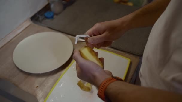 白人男性在自家厨房的桌子上剥去土豆皮 清洗土豆 煮开水了 食品准备的概念 不认识的人拿着刀和皮铲 — 图库视频影像