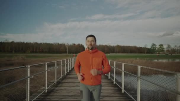 在寒冷的秋天 身穿橙色帽衫的男士们穿过国家公园 穿过荒野中的木桥 田径运动员在乡间的一座木桥上慢跑 锻炼身体 — 图库视频影像