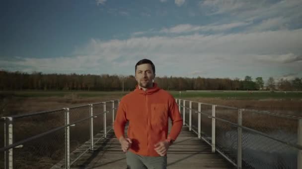 穿着橙色运动衫的慢跑者穿过斯堪的纳维亚半岛自然的木桥 运动员在寒冷的天气里跑过人行天桥 健康的生活方式在国家公园里的小径 — 图库视频影像