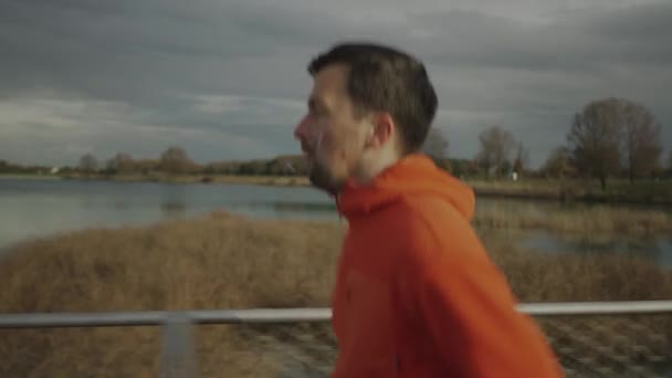 在寒冷的秋天 身穿橙色帽衫的男士们穿过国家公园 穿过荒野中的木桥 田径运动员在乡间的一座木桥上慢跑 锻炼身体 — 图库视频影像