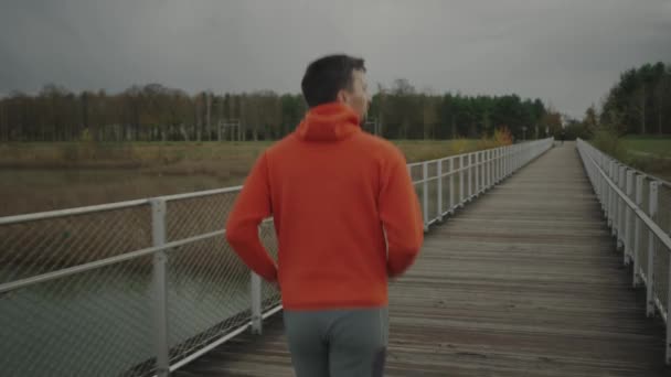 Мужчина Оранжевой Толстовке Бежит Через Национальный Парк Через Деревянный Мост — стоковое видео